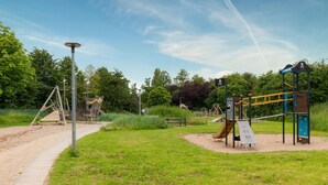 Ein Spielplatz mit verschiedenen Spielgeräten, darunter eine Rutsche und Klettergerüste, umgeben von Gras und Bäumen.