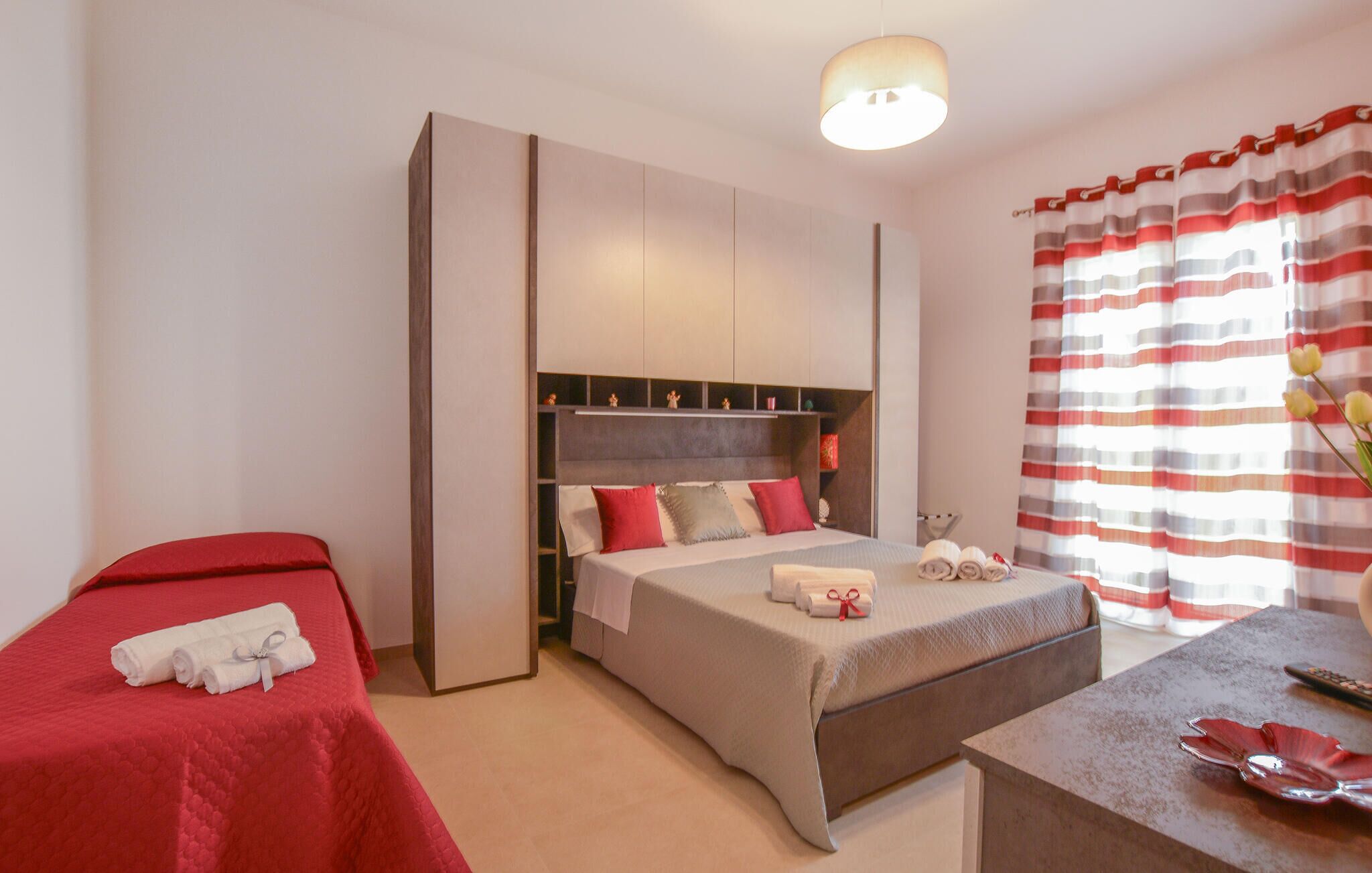 Een hotelkamer met een bed, nachtkastje, kledingkast en raam met gestreepte gordijnen.