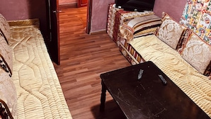Un salon comprenant un canapé, une table basse, un téléviseur et une porte donnant sur une autre pièce.