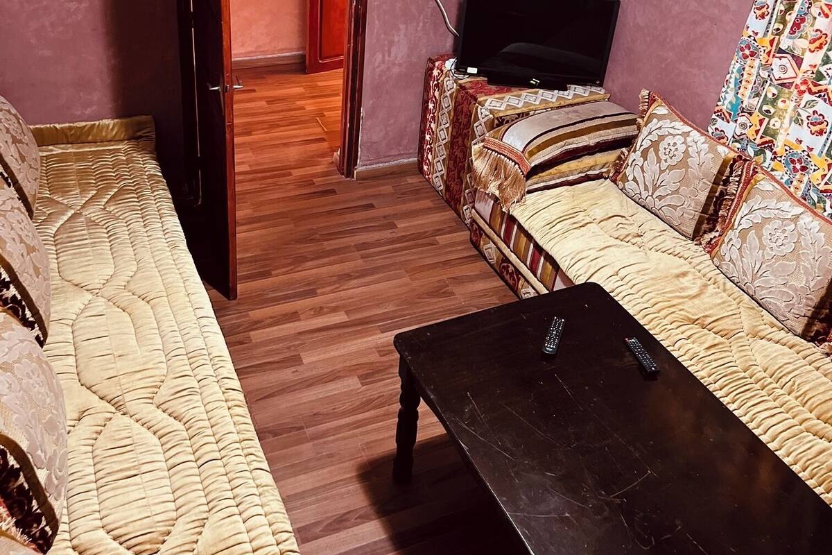 Una sala de estar con un sofá, una mesa de centro, un televisor y una puerta que da a otra habitación.