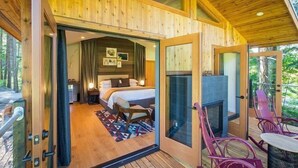 A wooden cabin with a bedroom, a fireplace, and a balcony with chairs. - ADA Luxury Tree House in Heart of Washington (Stevenson)