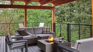 A covered outdoor deck with a sofa, chairs, a fire pit, and a table with a bottle and glass. - Premier Villa Escape: Nature, Dining, Fireside (Stevenson)