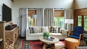 A living room with a sofa, a coffee table, a chair, a TV, and a window with curtains. - Premier Villa Escape: Nature, Dining, Fireside (Stevenson)