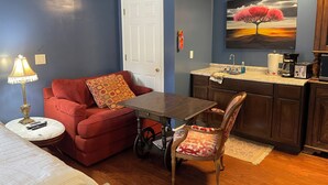 A compact living space with a kitchenette, a dining area with a table and chairs, a red sofa, and a lamp.