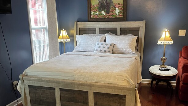 A bedroom with a bed, two bedside lamps, a zebra-patterned rug, a painting of an elephant, and a red chair.