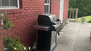 A red brick house with a black barbecue grill in the backyard.