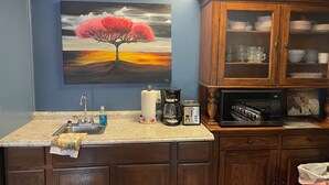 A kitchen with a granite countertop, a sink, a coffee maker, a toaster, and a microwave. There is a painting of a tree on the wall.
