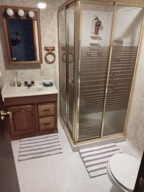 A bathroom with a wooden vanity, a mirror with lights, a glass shower enclosure, and a toilet.