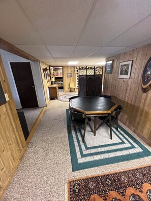 A room with a wooden floor, a round table with chairs, a patterned rug, and wooden paneling on the walls.