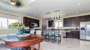 A spacious kitchen with dark wooden cabinets, a central island with bar stools, a large wooden dining table, and a modern stainless steel refrigerator. - Hilo Hibiscus Vacation Home 3 bedrooms  (Hilo)