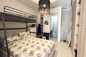 A bedroom with bunk beds, a bedside table, a hanging light fixture, a wardrobe, and a bathroom with a shower curtain.