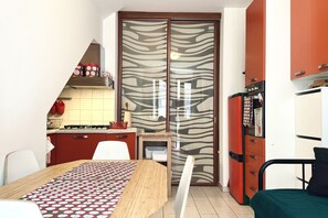 A compact kitchen with a gas stove, a refrigerator, and a microwave. There is a dining table with a patterned tablecloth.