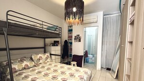 Une chambre avec un lit superposé, une couvre-lit à motifs, un luminaire suspendu et une salle de bain visible à travers une porte ouverte.