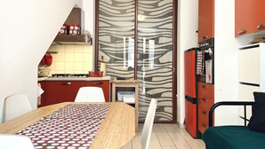 Une cuisine compacte équipée d’une cuisinière à gaz, d’un réfrigérateur et d’un four à micro-ondes. On y trouve une table à manger recouverte d’une nappe à motifs.
