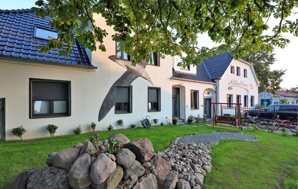 A two-story building with a blue tiled roof, a large tree in front, and a stone wall in the foreground. - Amazing apartment in Großenbrode with WiFi (Großenbrode)