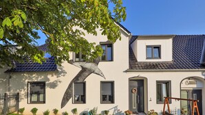 Ein zweistöckiges Haus mit einem großen Baum davor, einer Schaukel und einem kleinen Garten.