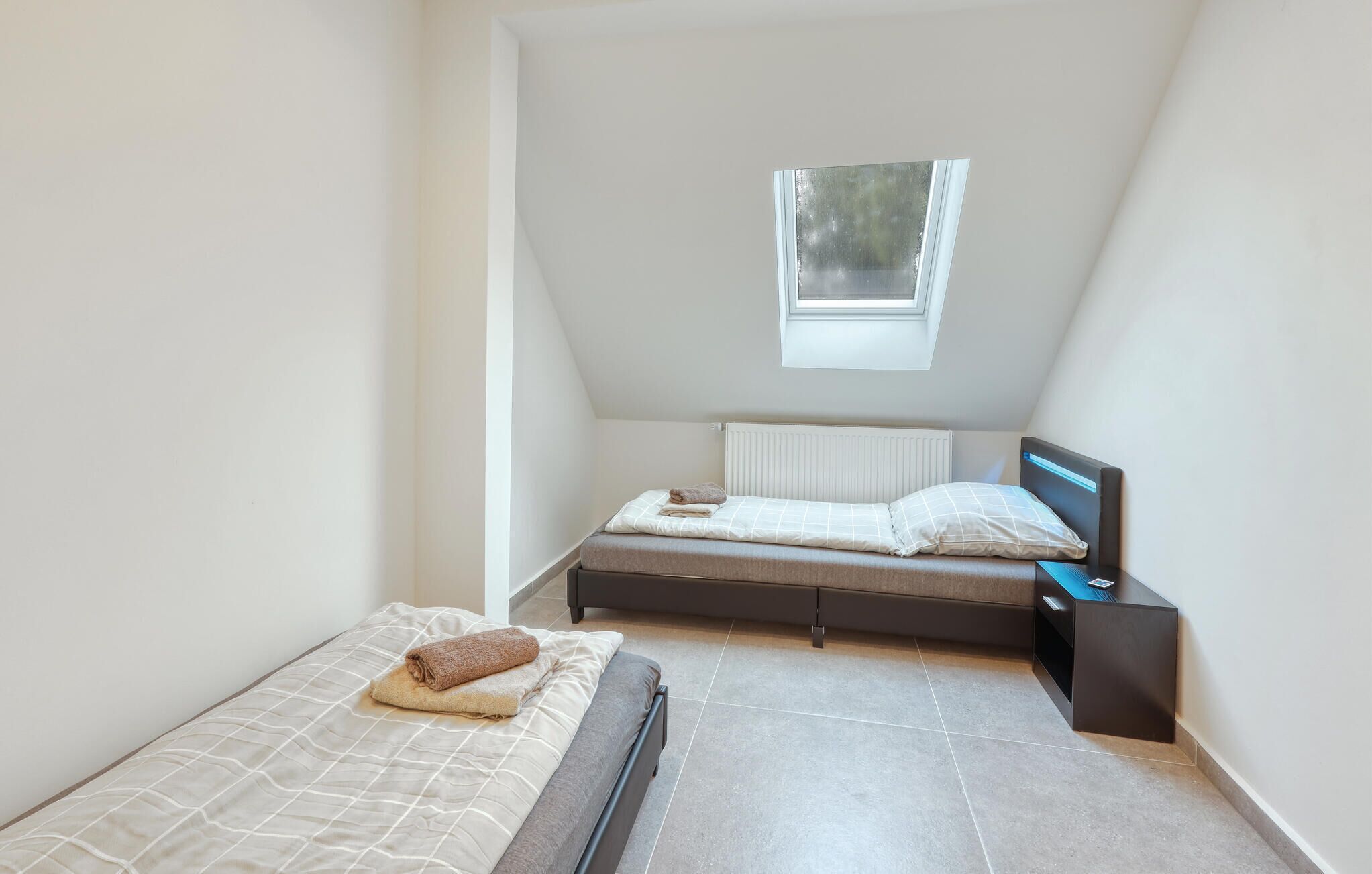 Una camera da letto piccola e moderna con un soffitto spiovente, un lucernario, un letto con testiera e un comodino.