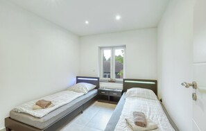 A small, bright room with two single beds, a window with a view of the outside, and a door with a handle. - Amazing apartment in Großenbrode with WiFi (Großenbrode)