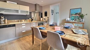 Una cocina moderna con electrodomésticos de acero inoxidable, una mesa de comedor de madera preparada para cuatro personas y vista al mar a través de una ventana.