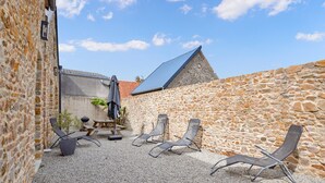 Un patio con paredes de piedra, una pérgola de madera y mobiliario exterior.