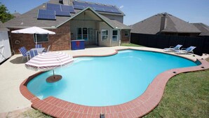 A backyard with a swimming pool, a covered patio area, and solar panels on the roof. - Huge 4BR w/ Pool + Grill | Near Lakes and Harbor! (Royse City)