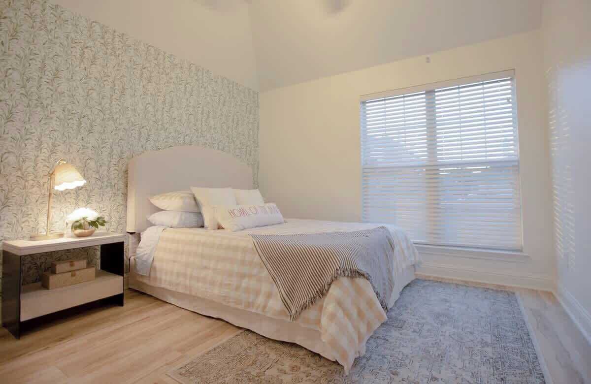 A bedroom with a bed, bedside tables, a lamp, and a window with blinds.