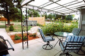 Un patio cubierto con un conjunto de asientos, una parrilla y un jardín con girasoles.
