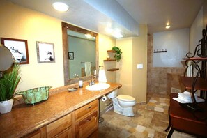 Un baño con encimera de granito, un lavabo blanco, un espejo, un inodoro y una zona de ducha.