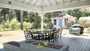A covered patio with a table and chairs, surrounded by a garden and a small house. - Homerun Hideaway! Beach/OWA/Sports/Shopping (Foley)