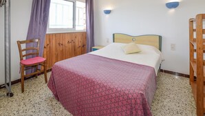 A bedroom with a bed, a chair, a window, and a wall-mounted light fixture. - Lovely apartment in Calvi with WiFi (Calvi)