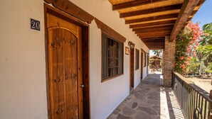 A covered corridor with stone flooring, wooden doors, and a balcony with a metal railing. - Rancho Maria Teresa (Valle de Guadalupe)