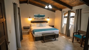 A bedroom with a bed, bedside tables, a bench, a chair, a painting, and a window with curtains. - Rancho Maria Teresa (Valle de Guadalupe)