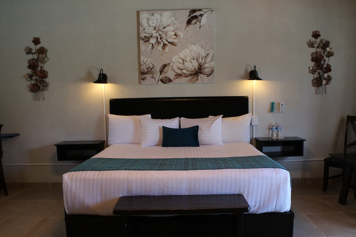 A neatly arranged hotel room with a large bed, bedside tables, a bedside lamp, a small table, and a wall-mounted artwork.