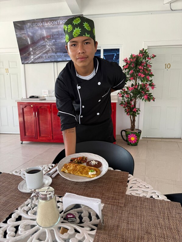 A person seated at a table with a plate of food, a coffee cup, and a decorative pitcher.