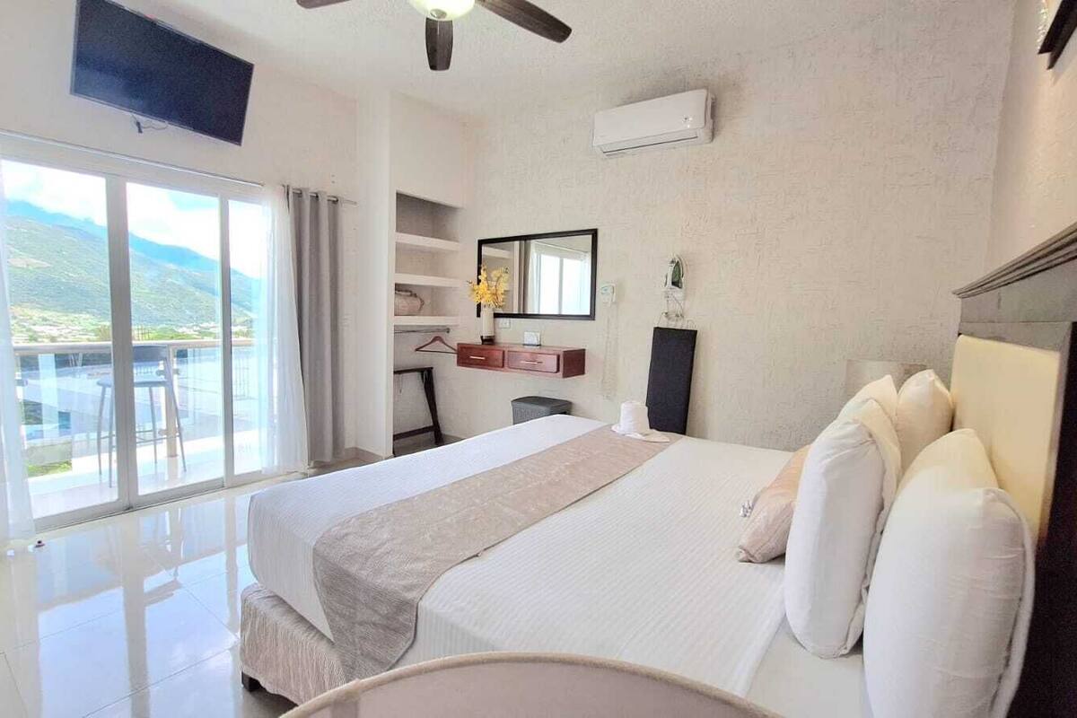 Una habitación de hotel con cama, televisor, escritorio y vistas al exterior.
