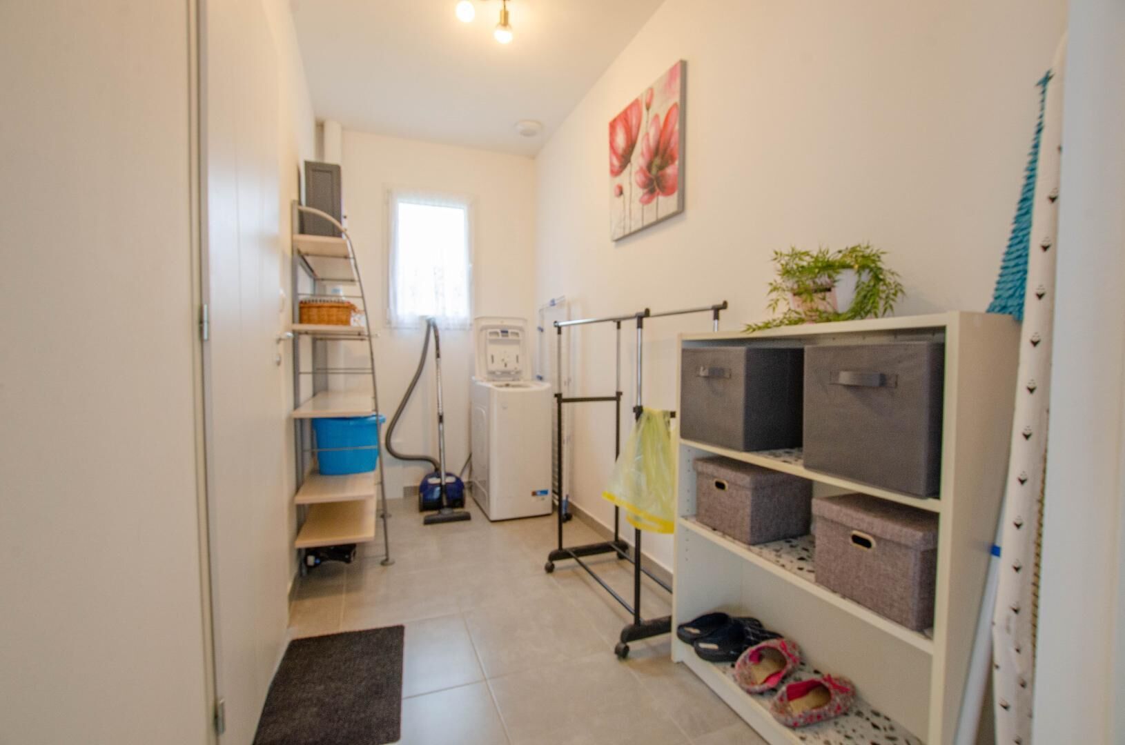 A laundry room with a washing machine, drying rack, shelves with baskets, and a small plant.