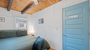 Une chambre à coucher avec un lit, une fenêtre avec des stores, une porte et un tableau accroché au mur.