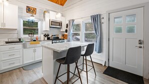 Une cuisine avec des meubles blancs, un îlot central doté de tabourets, un four à micro-ondes et une cuisinière.