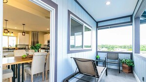 Una cocina moderna con armarios blancos, un comedor con mesa y sillas de madera, y un balcón con una silla y plantas en macetas.