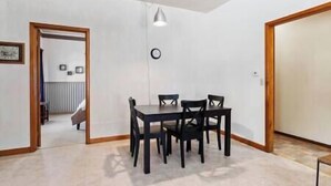 A dining area with a table and chairs, a clock on the wall, and a door leading to another room. - Depot Suite (Elkader)