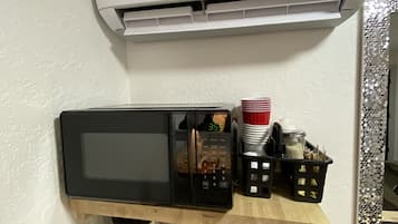 A kitchen with a microwave, a coffee maker, and a shelf with kitchen utensils.