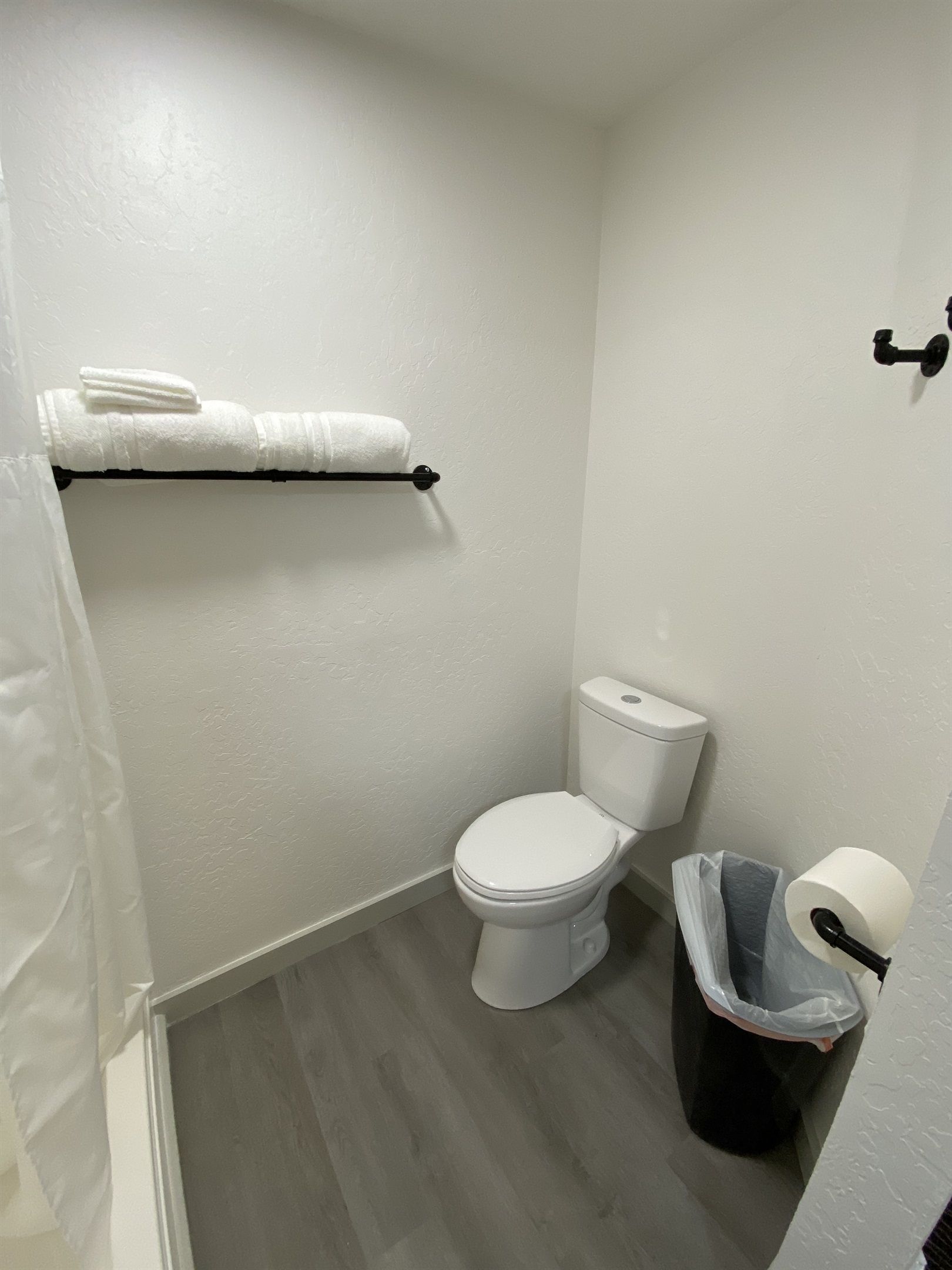Ein kleines Badezimmer mit Toilette, Handtuchhalter mit Handtüchern, einem Papierkorb und einem Toilettenpapierhalter.