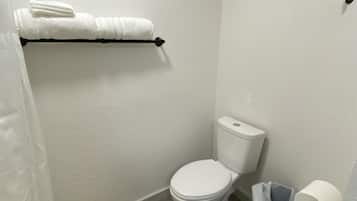 Ein kleines Badezimmer mit Toilette, Handtuchhalter mit Handtüchern, einem Papierkorb und einem Toilettenpapierhalter.