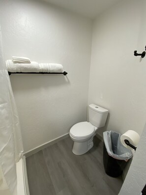 Ein kleines Badezimmer mit Toilette, Handtuchhalter mit Handtüchern, einem Papierkorb und einem Toilettenpapierhalter.
