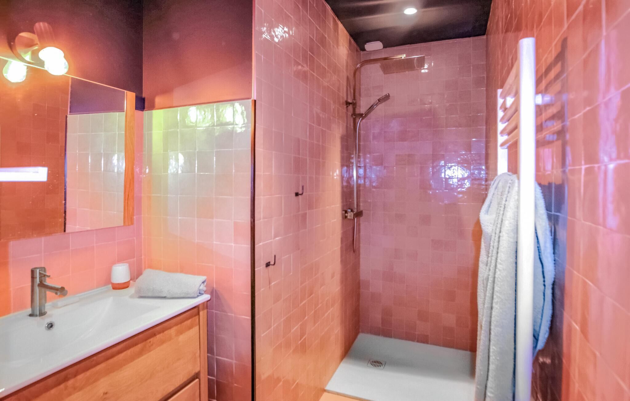 A bathroom with pink tiles, a sink, a mirror, a shower, and a towel rack.