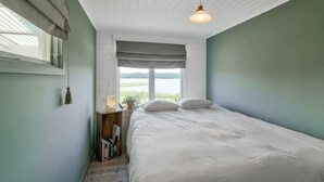 Une chambre à coucher avec un lit, une table de chevet avec une lampe, une fenêtre donnant sur l’extérieur et un luminaire suspendu.