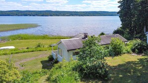 Une maison avec un toit en métal, entourée d’une végétation luxuriante et bordée d’un lac.