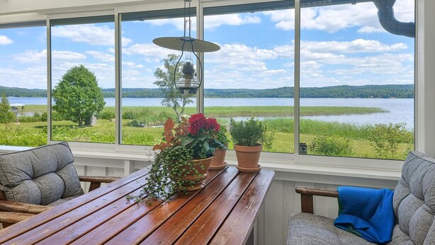 Une véranda avec de grandes fenêtres donnant sur un lac, des meubles en bois et des plantes en pot.
