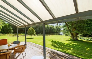 A covered patio with a table and chairs, overlooking a well-maintained lawn and trees. - 4 bedroom gorgeous home in Varde (Varde)
