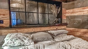 Een houten kamer met een bed, kussens en een raam met een decoratieve plant.